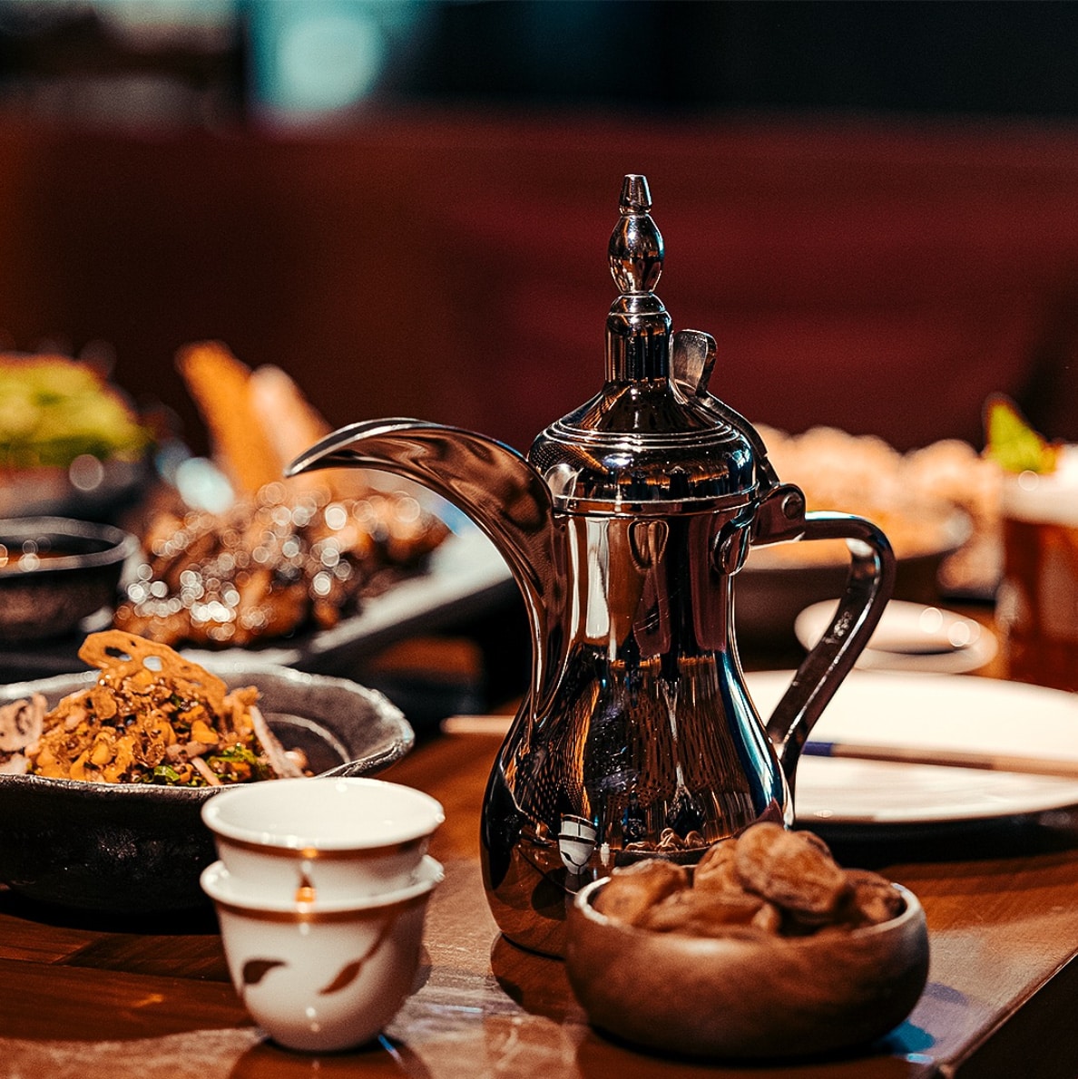 Traditional Middle Eastern dining setting featuring a shiny metal teapot and cup with various dishes in the background