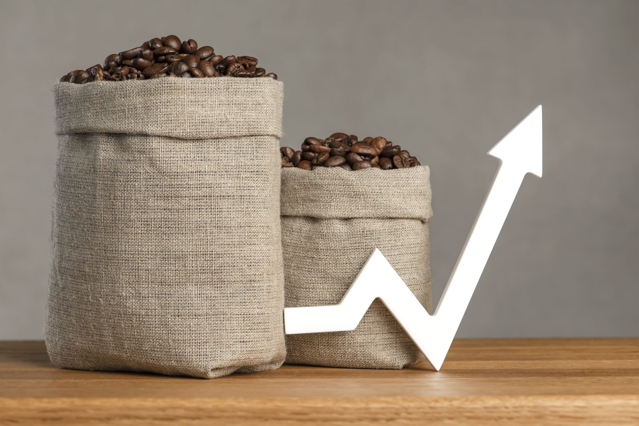 Two burlap sacks filled with coffee beans placed on a wooden surface, accompanied by a white upward arrow symbolising market growth in the Middle East coffee industry.