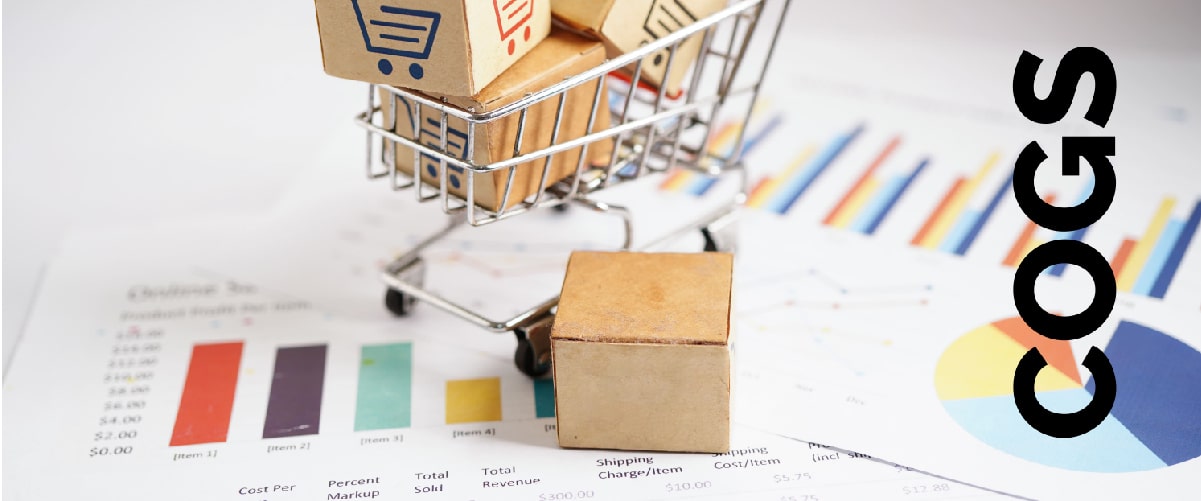 Mini shopping cart with cardboard boxes placed on financial charts, representing cost of goods sold (COGS) analysis