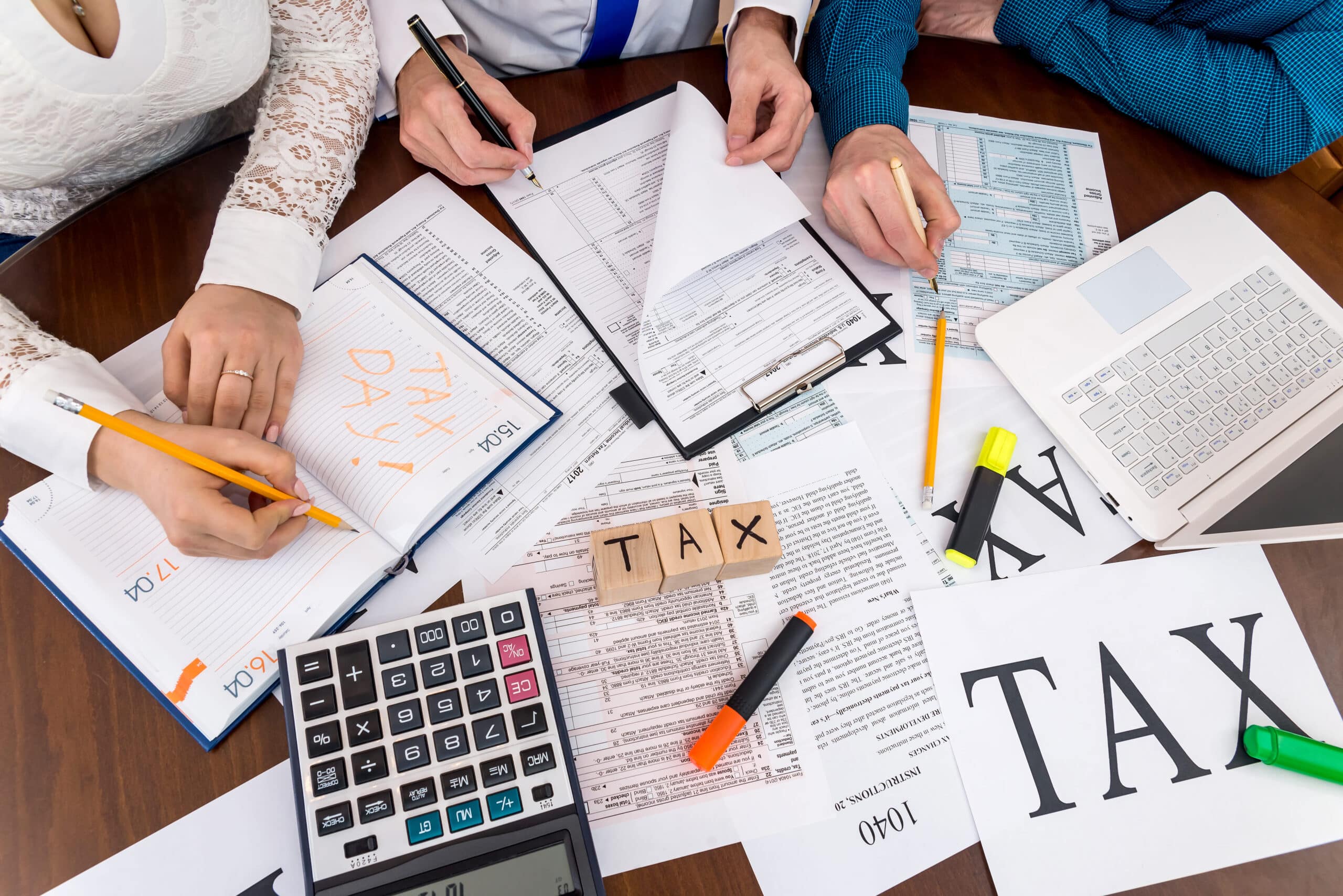Three employees working together at an office table, discussing tax regulations for bars and nightclubs, with documents and a laptop on the table.