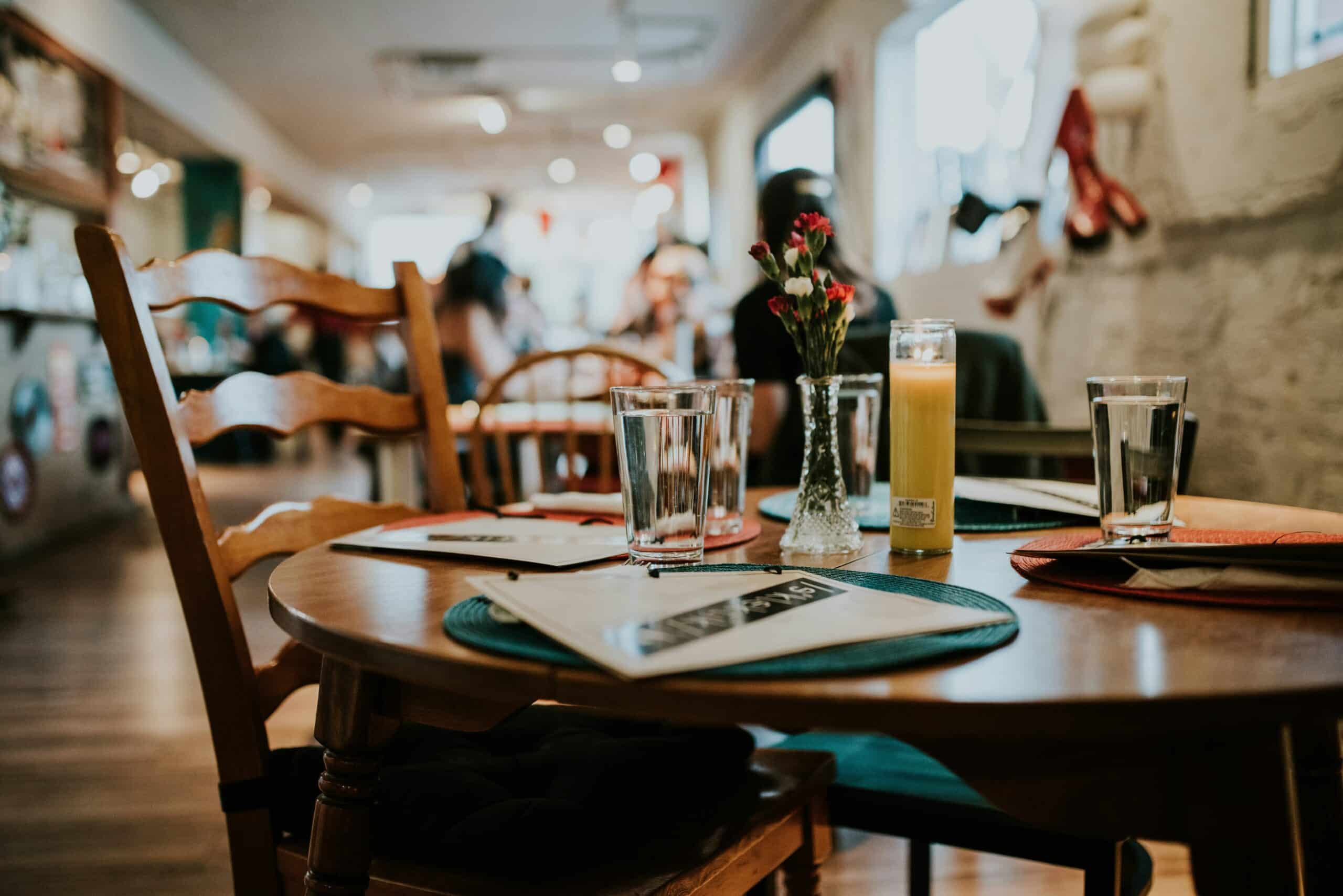 Cozy restaurant table setup with menus, glasses of water, a small vase with flowers, and a candle, representing a welcoming atmosphere in the hospitality industry. Relevant for topics like Hospitality Accounting and restaurant management.