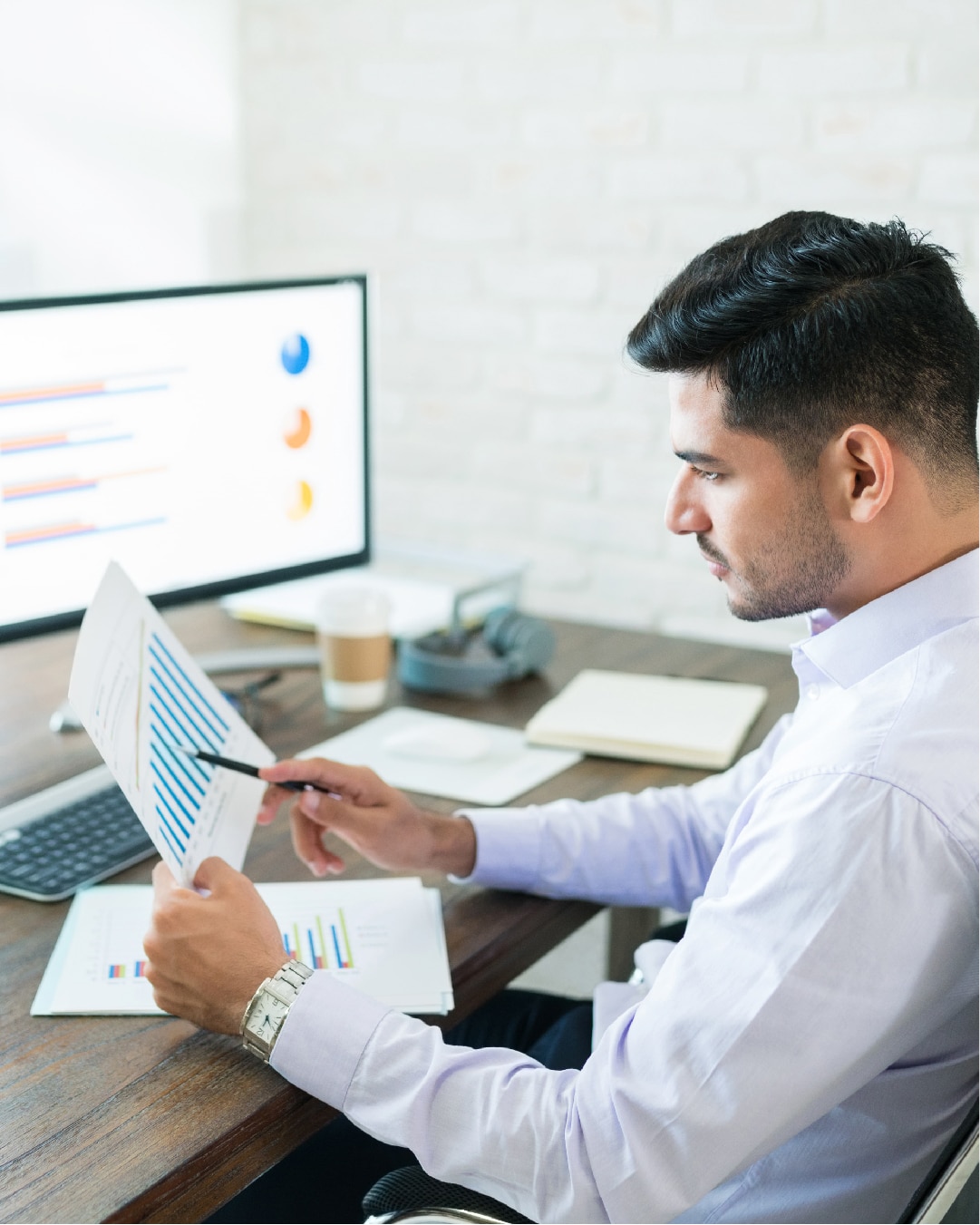Man at computer desk analyzing data on the paper he has taken out from hospitality business software 