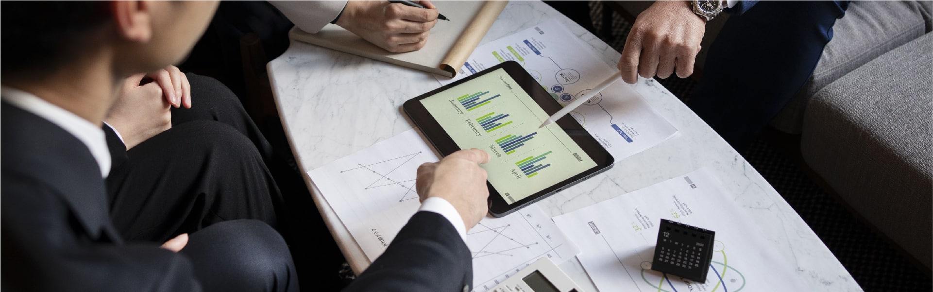 Business professionals examining data and graphs on a tablet, discussing service charges in the UAE hospitality industry, emphasising financial analysis and strategic planning.