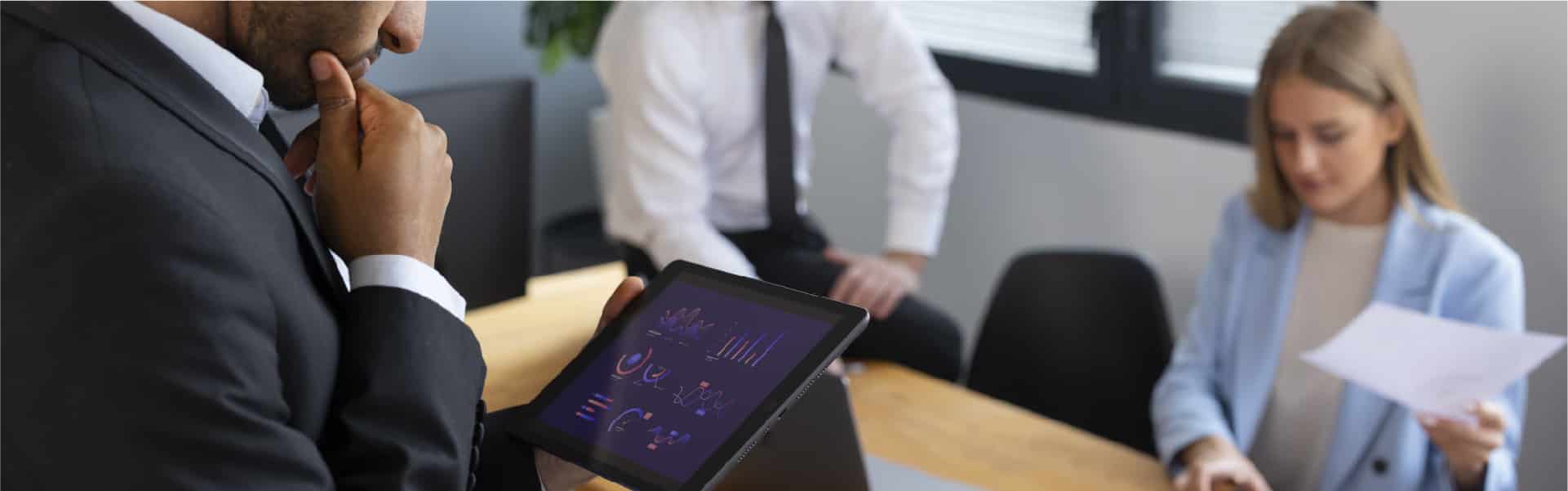 Business professionals in a meeting, with a man using a tablet to discuss VAT and service charges, illustrating the use of technology and tools in managing VAT for UAE hospitality