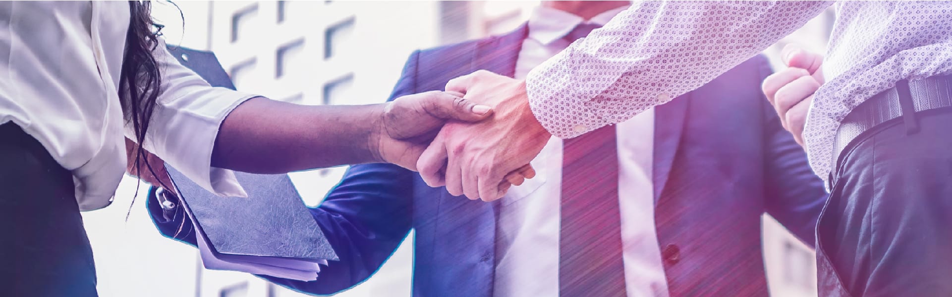Business professionals shaking hands in agreement, symbolizing partnership and collaboration, with a modern office building in the background.