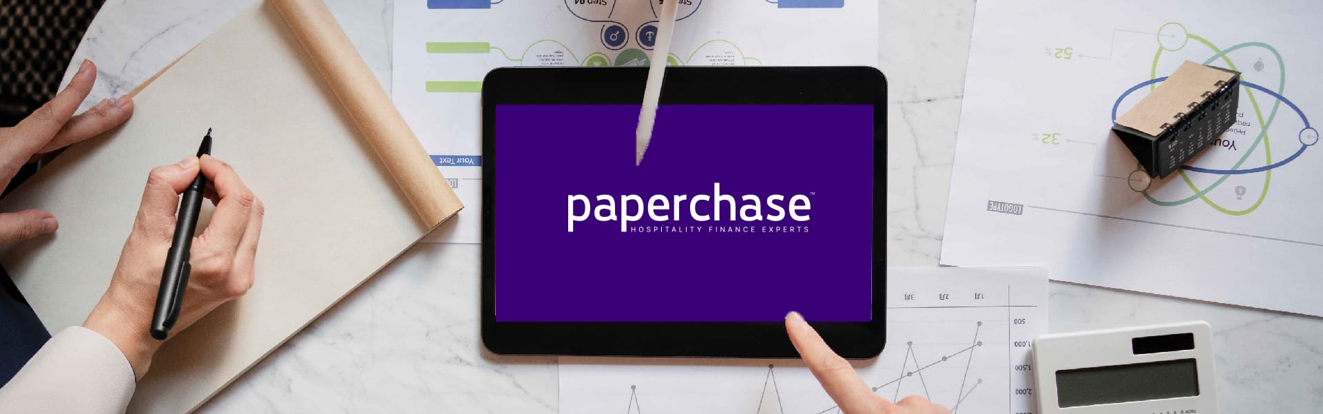 Tablet displaying 'Paperchase Hospitality Finance Experts' on a desk surrounded by business charts, a calculator, a notepad, and a hand writing notes, symbolizing financial planning and analysis in hospitality.